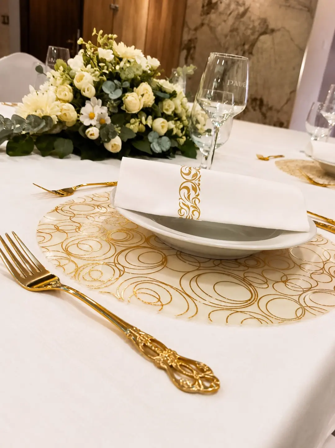 Biely tanier a obrúsok so zlatým ornamentom pri kvetinovej dekorácii vo WX Hoteli